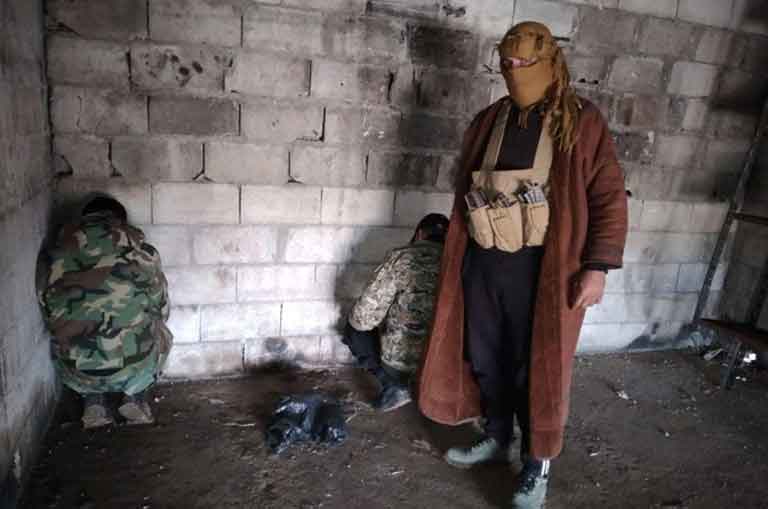 Боевик фотографируется на фоне взятых в плен сирийских военнослужащих